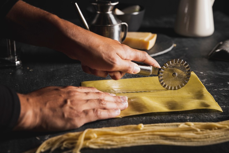 Una persona taglia con una rotella l'impasto della pasta fresca
