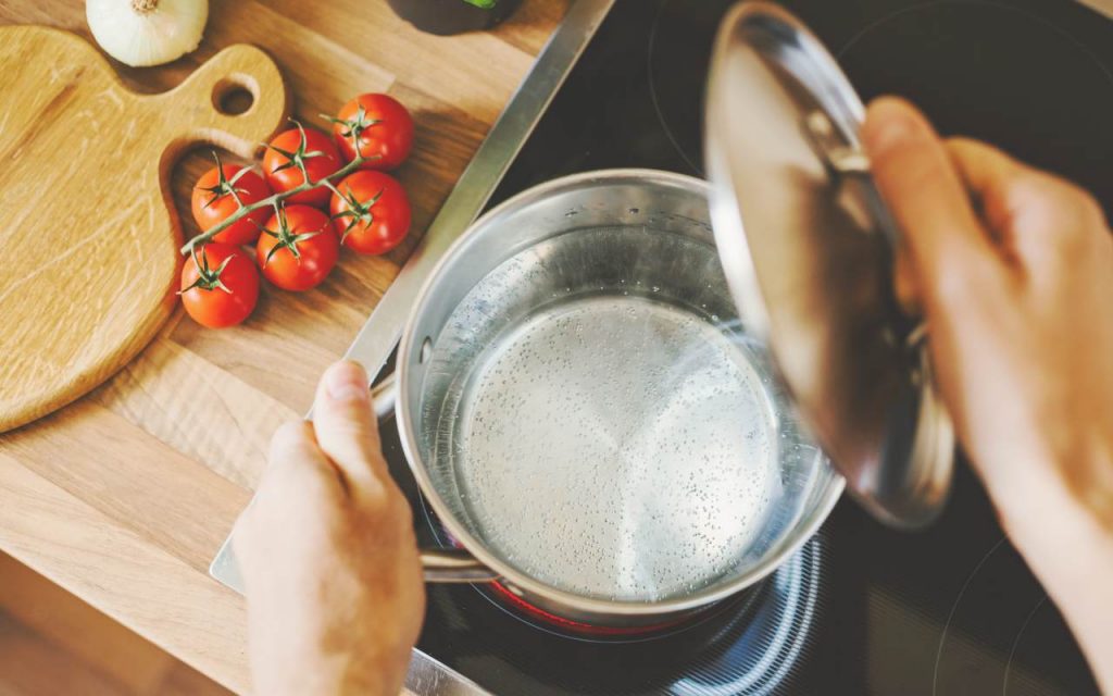 Una persona mette una pentola con dell'acqua sul fuoco in cucina
