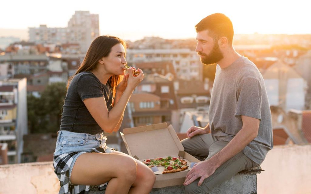 Un ragazzo e una ragazzo mangiano una pizza in città