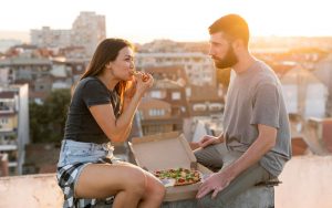 Un ragazzo e una ragazzo mangiano una pizza in città